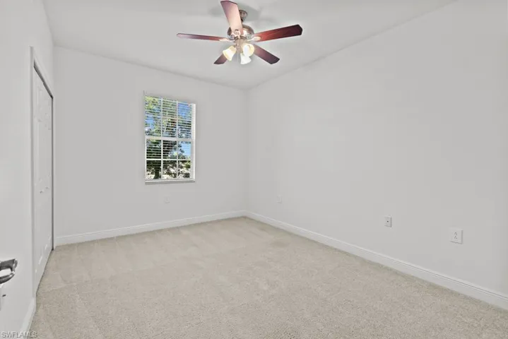 Spare room featuring a ceiling fan, light colored carpet, and baseboards