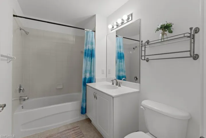 Bathroom featuring shower / bathtub combination with curtain, vanity, toilet, and tile patterned floors