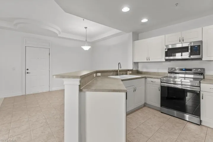 Kitchen featuring a peninsula, white cabinets, stainless steel appliances, and hanging light fixtures