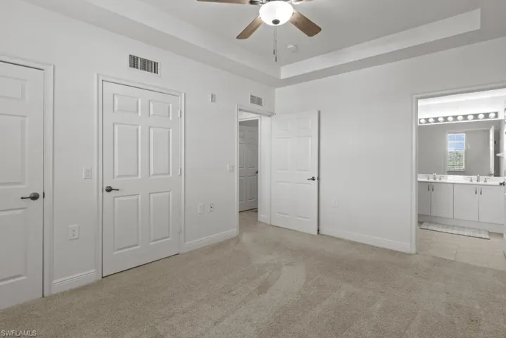 Unfurnished bedroom featuring light carpet, a tray ceiling, connected bathroom, and visible vents