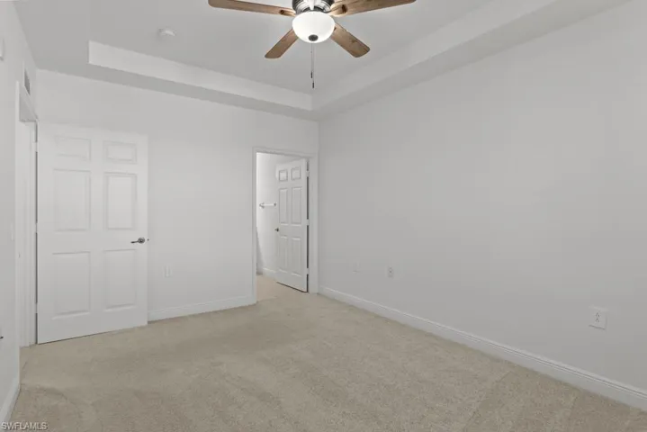 Unfurnished bedroom featuring light carpet, a raised ceiling, and baseboards