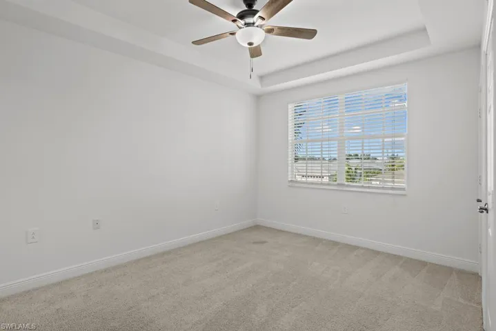 Carpeted empty room featuring a raised ceiling, a ceiling fan, and baseboards