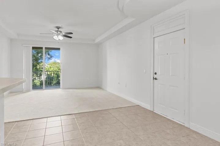 Spare room with baseboards, a raised ceiling, light colored carpet, ceiling fan, and light tile patterned flooring