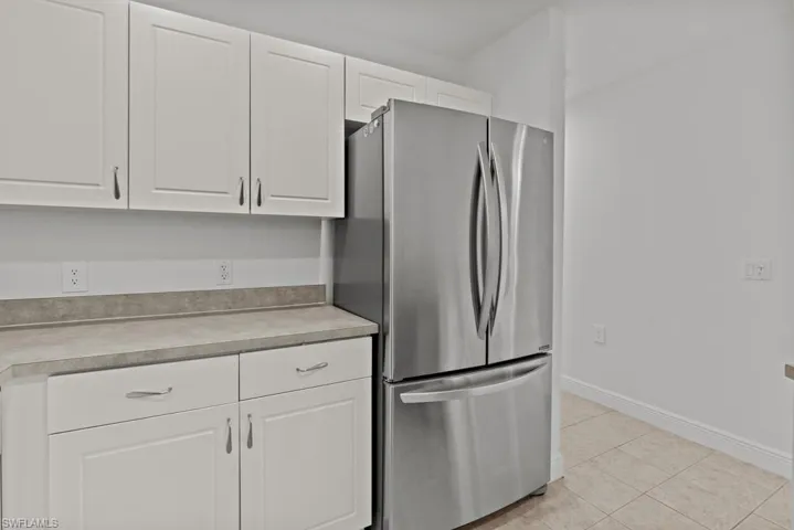 Kitchen featuring freestanding refrigerator, white cabinets, light countertops, and light tile patterned floors
