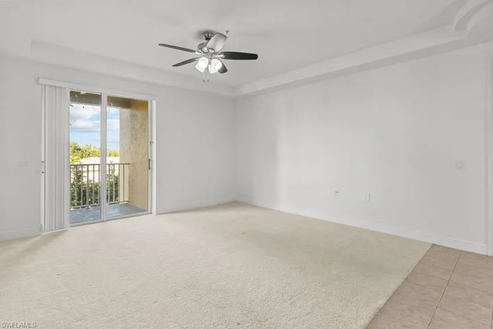 Spare room with a ceiling fan, a tray ceiling, light colored carpet, and baseboards