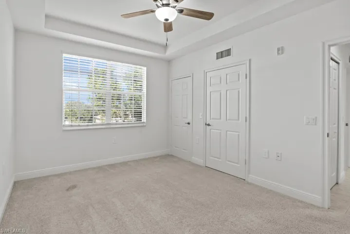 Unfurnished bedroom with light carpet, a tray ceiling, visible vents, and baseboards