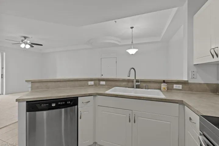 Kitchen featuring white cabinets, dishwasher, light countertops, pendant lighting, and a sink