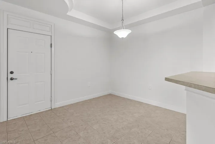 Unfurnished dining area with a raised ceiling, light tile patterned flooring, and baseboards