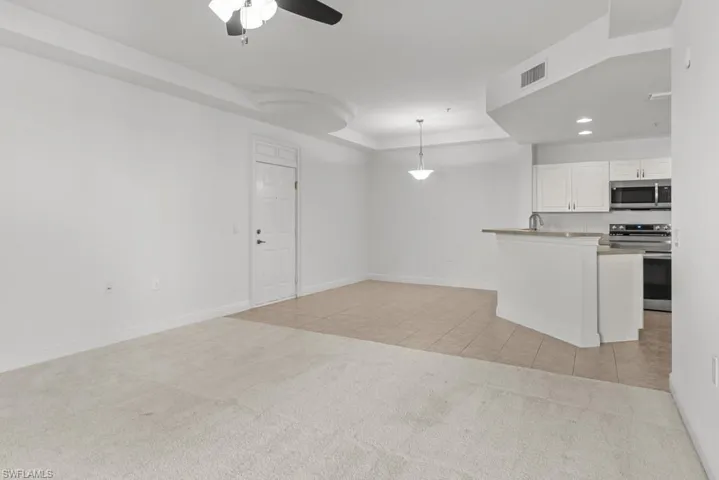 Unfurnished living room featuring light tile patterned floors, light carpet, visible vents, baseboards, and a raised ceiling