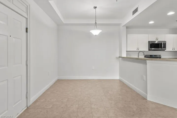 Kitchen with baseboards, stainless steel microwave, decorative light fixtures, light countertops, and white cabinetry