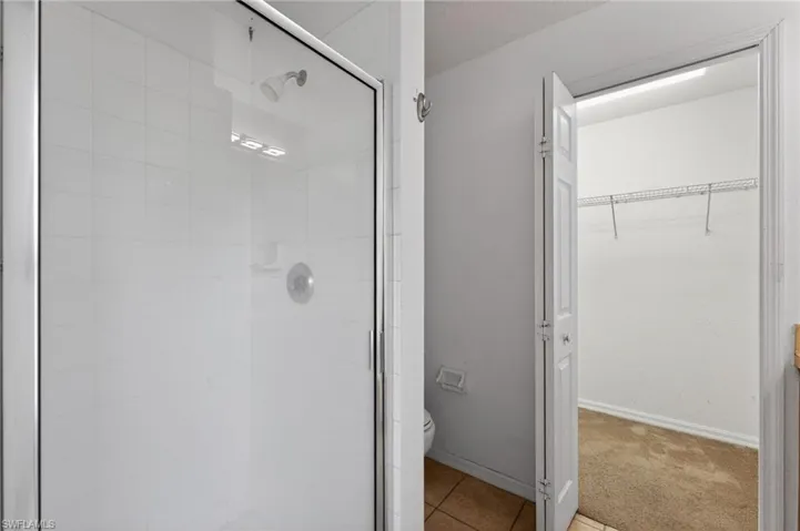 Glass-enclosed shower with white tiled walls and a chrome showerhead
