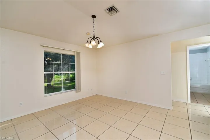 Spacious interior room featuring light-toned tile flooring, a multi-pane window, and a five-light chandelier