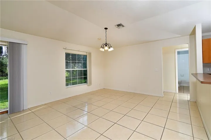 Spacious room featuring neutral-toned tile flooring, a large window, and a sliding glass door