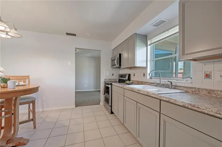 Kitchen featuring gray cabinets, backsplash, light tile floors, sink, and appliances with stainless steel finishes