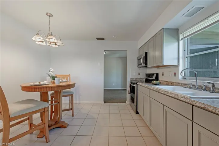 Kitchen featuring stainless steel appliances, decorative light fixtures, a notable chandelier, sink, and light tile flooring
