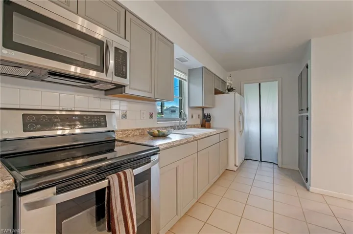 Kitchen with tasteful backsplash, gray cabinets, light tile floors, sink, and appliances with stainless steel finishes