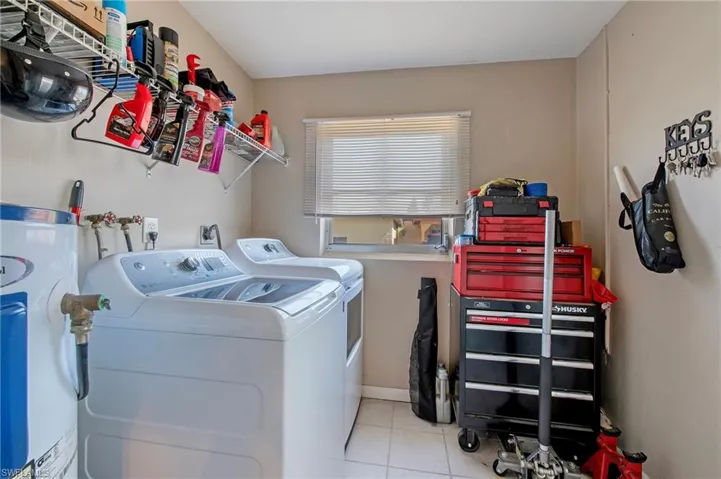 Washroom with washing machine and clothes dryer, hookup for a washing machine, electric dryer hookup, water heater, and light tile flooring