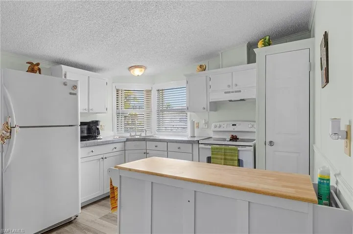 Kitchen featuring white appliances, a textured ceiling, white cabinets, under cabinet range hood, and a sink