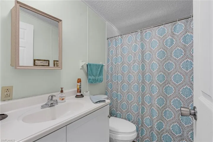 Bathroom featuring toilet, curtained shower, vanity, and a textured ceiling