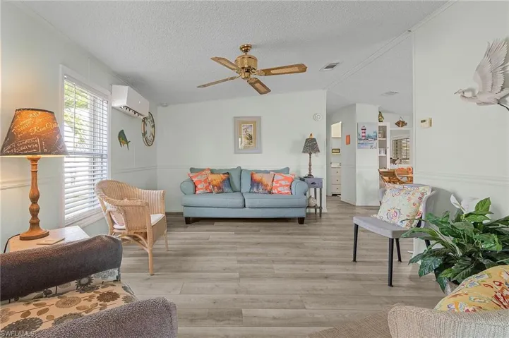 Living area with light wood-style floors, ceiling fan, a textured ceiling, visible vents, and a wall mounted AC