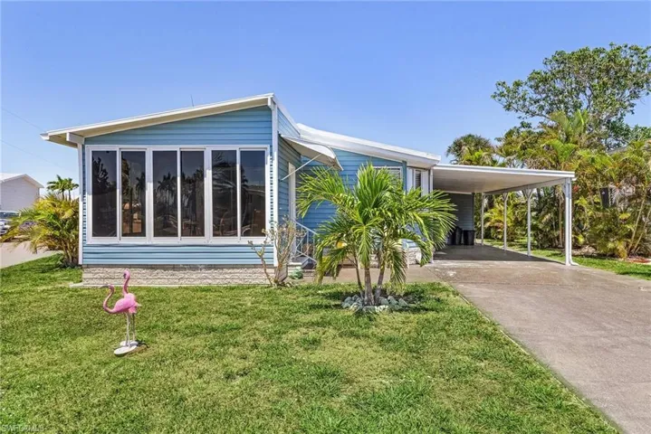 View of property exterior featuring a sunroom, a carport, a yard, and driveway