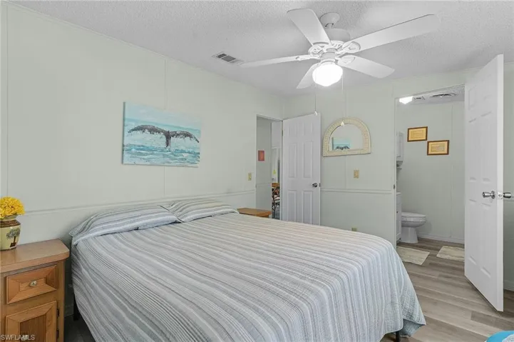 Bedroom with light wood-type flooring, ensuite bathroom, visible vents, and a textured ceiling