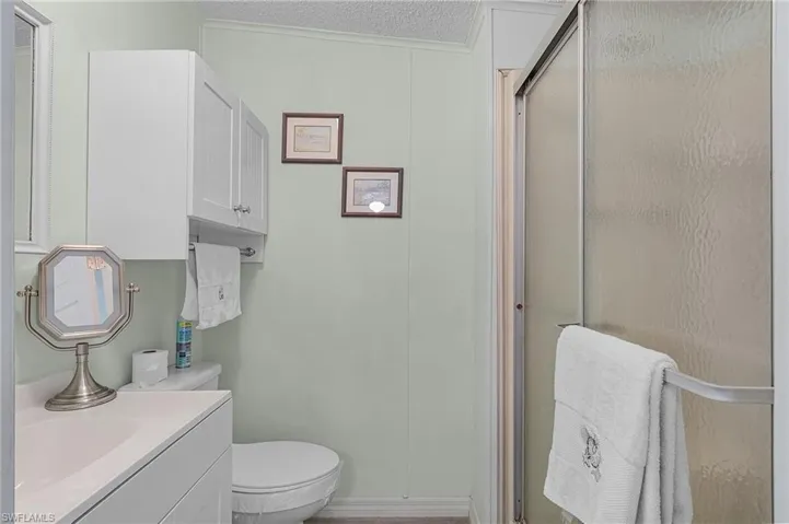 Bathroom with toilet, a textured ceiling, a stall shower, and vanity