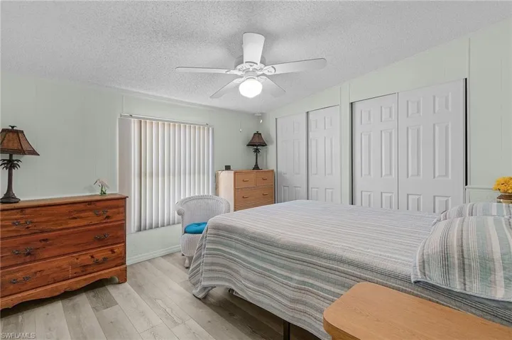 Bedroom featuring a textured ceiling, wood finished floors, a ceiling fan, and multiple closets