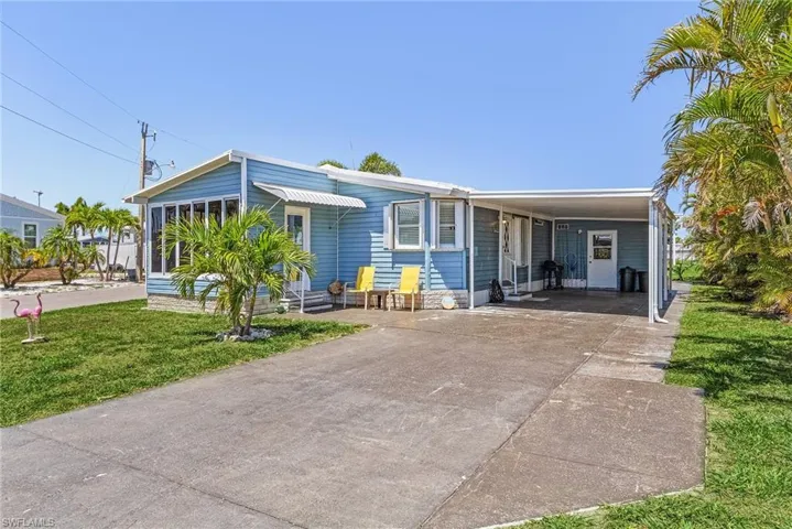 View of front of house with entry steps, a front lawn, an attached carport, and concrete driveway