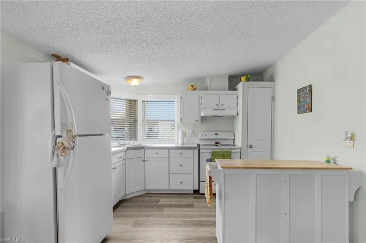 Kitchen with white appliances, a textured ceiling, crown molding, under cabinet range hood, and light wood finished floors