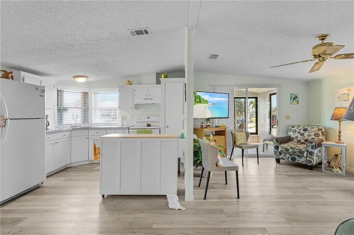 Kitchen with white appliances, light wood-style flooring, a textured ceiling, visible vents, and under cabinet range hood