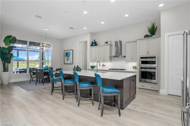 Kitchen with light hardwood / wood-style floors, stainless steel appliances, wall chimney exhaust hood, a breakfast bar area, and a kitchen island with sink