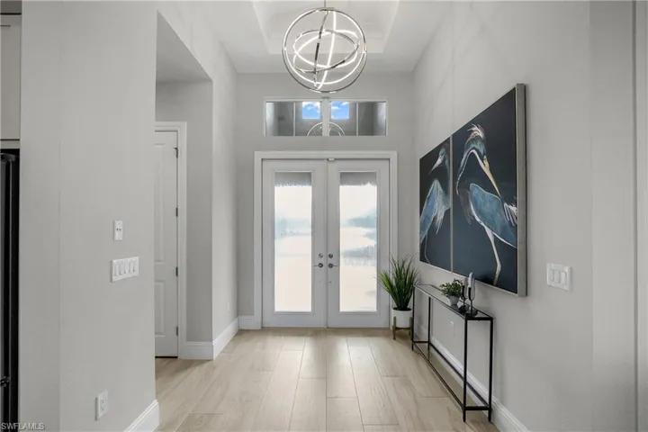 Foyer featuring high ceilings, hurricane impact glass front doors, modern and stunning chandelier.