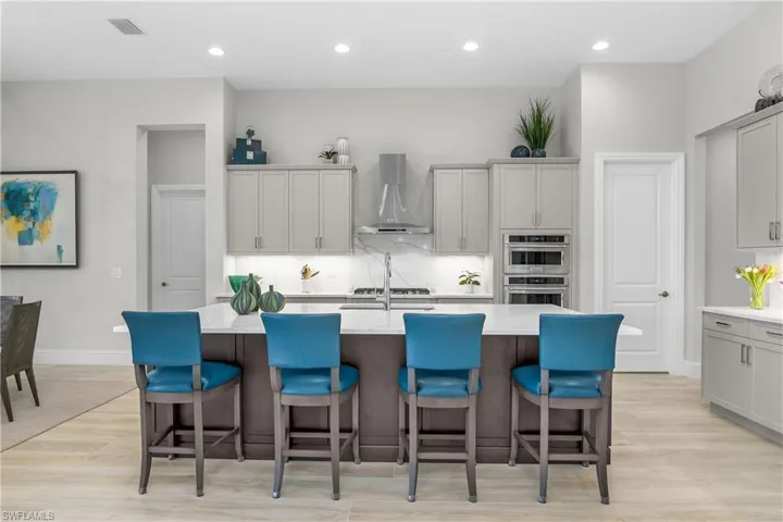 Kitchen featuring wall chimney exhaust hood, a center island with sink, light wood-type flooring, and a breakfast bar