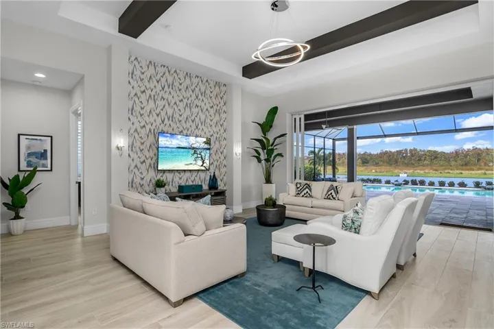 Living room featuring soaring ceilings with wood beams and custom lighting, feature wall, and magnificent views of the outdoor space, water, and preserve beyond.