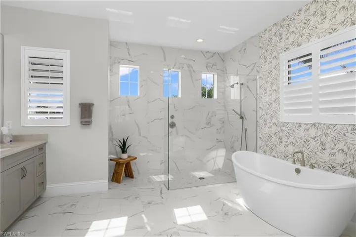 Bathroom featuring dual sink vanity, walk in  frameless glass shower, stand alone soaking tub and plantation shutters.