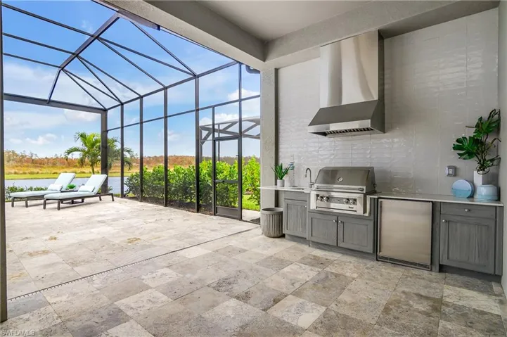 View of patio with area for grilling, a grill, sink, a water view, and glass enclosure