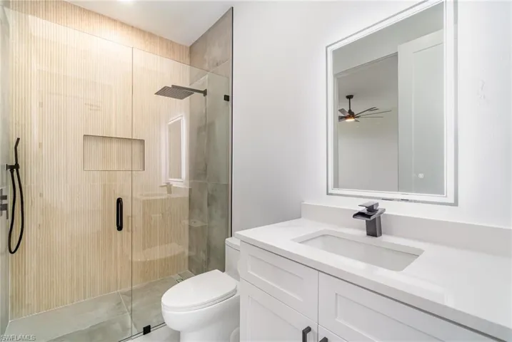 Bathroom with a shower with door, toilet, vanity, and ceiling fan