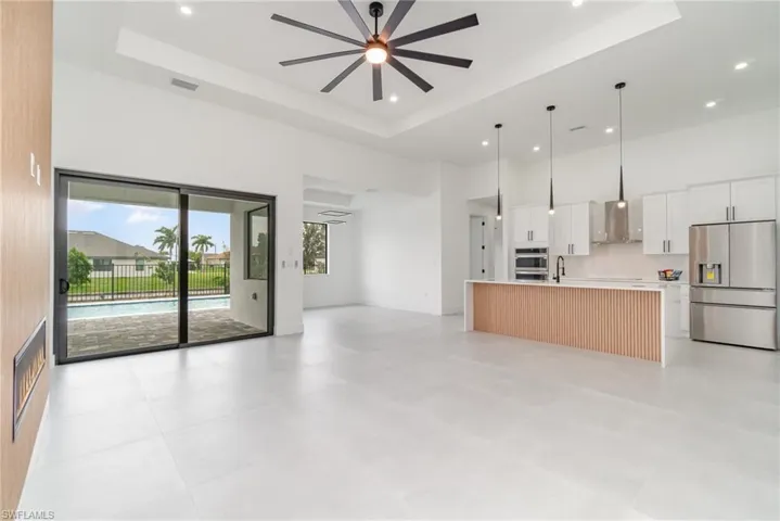 Unfurnished living room with light tile patterned flooring, ceiling fan, a towering ceiling, and a tray ceiling