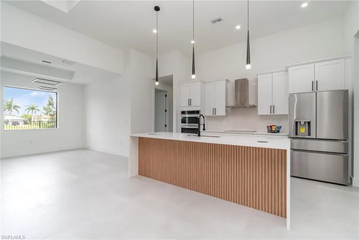 Kitchen featuring light tile patterned floors, white cabinets, an island with sink, wall chimney exhaust hood, and appliances with stainless steel finishes