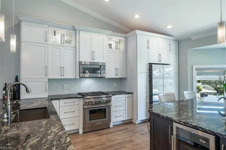 Kitchen featuring appliances with stainless steel finishes, white cabinets, decorative light fixtures, and wine cooler