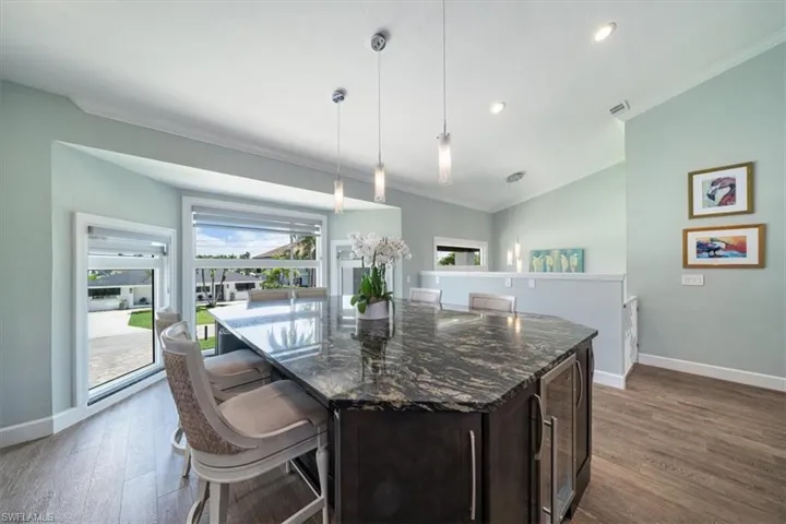 Kitchen with dark stone countertops, wine cooler, hardwood / wood-style floors, crown molding, and pendant lighting
