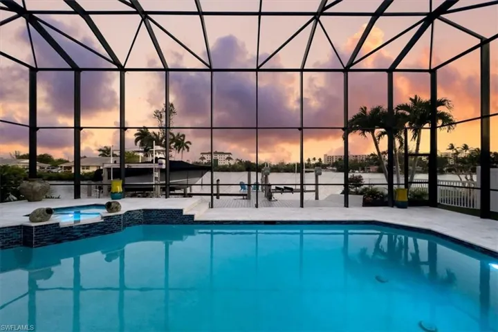 Pool at dusk featuring a water view, a patio, and glass enclosure