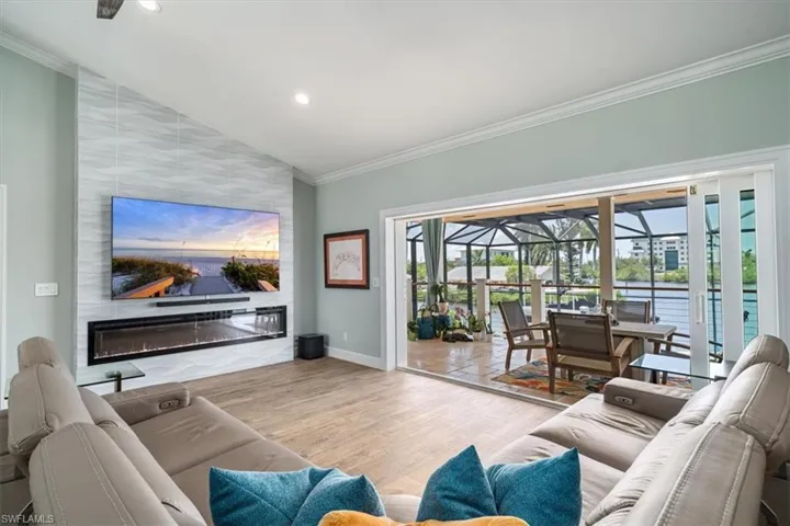Living room featuring light wood-type flooring, a large fireplace, vaulted ceiling, a water view, and crown molding