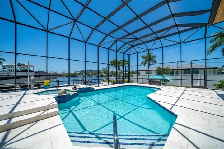 View of pool featuring an in ground hot tub, a patio area, a water view, and glass enclosure