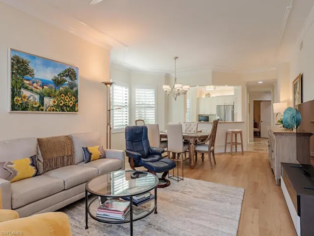 Living room with a notable chandelier, light wood-type flooring, visible vents, and crown molding