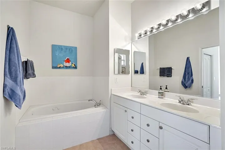 Full bath with double vanity, tile patterned flooring, and a jetted tub