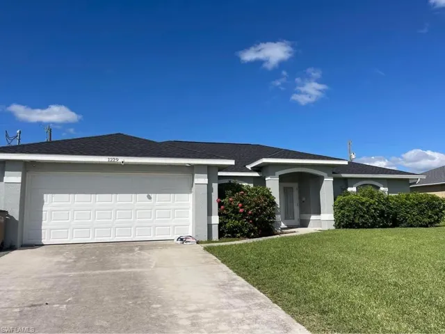 Ranch-style home with a front yard, concrete driveway, stucco siding, and roof with shingles