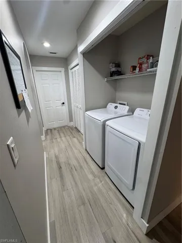 Dedicated laundry area featuring a washer and dryer, light wood-finish flooring, and a wire storage shelf