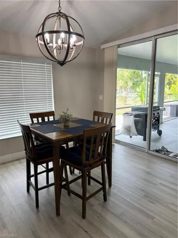 Vaulted ceiling with an orb chandelier, light wood-finish flooring, and sliding glass doors leading to an outdoor screened patio